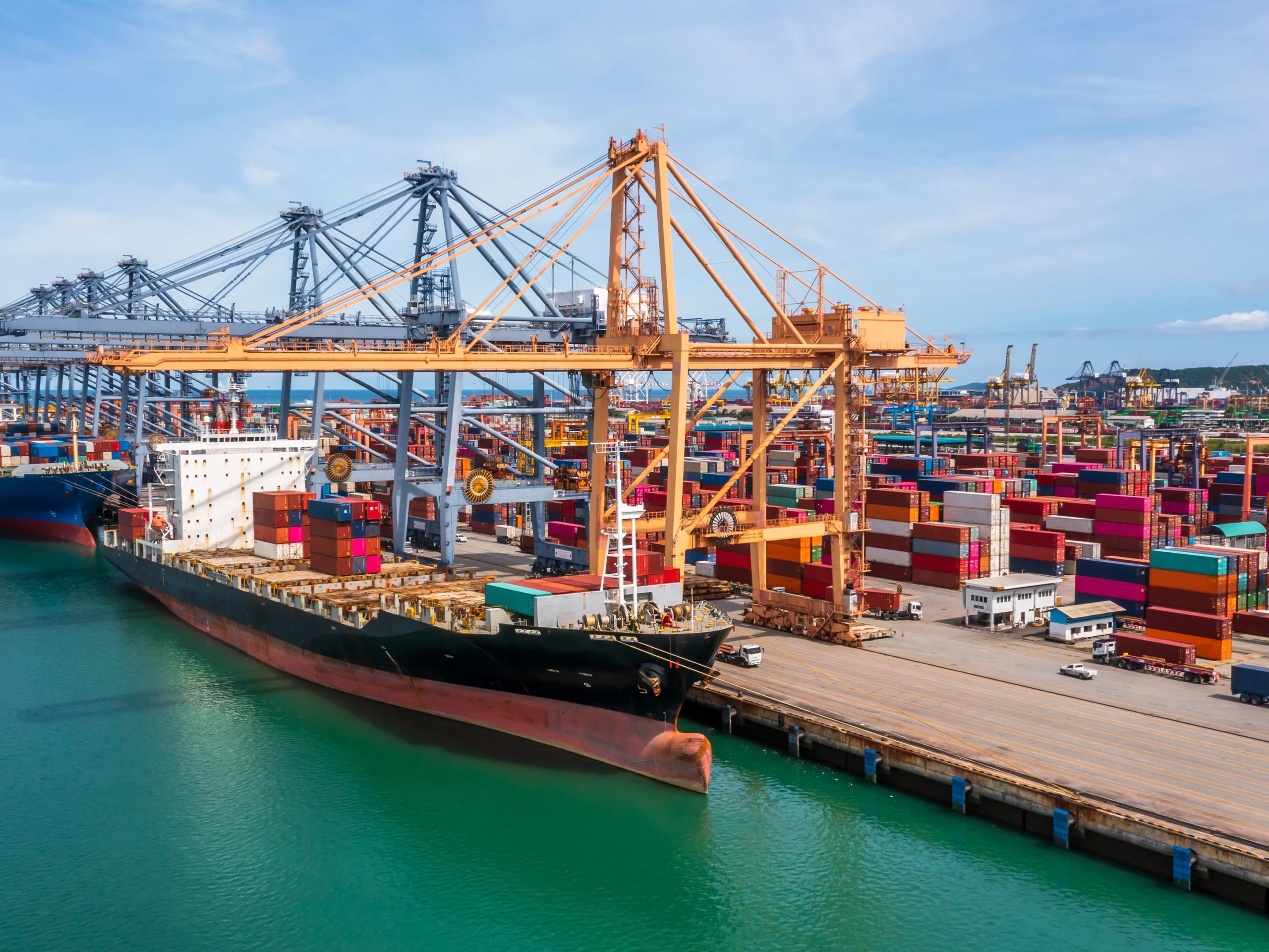 ¿Qué hace un agente de carga? Buque de carga atracado en un puerto internacional mientras grúas trasladan contenedores para operaciones de importación y exportación.